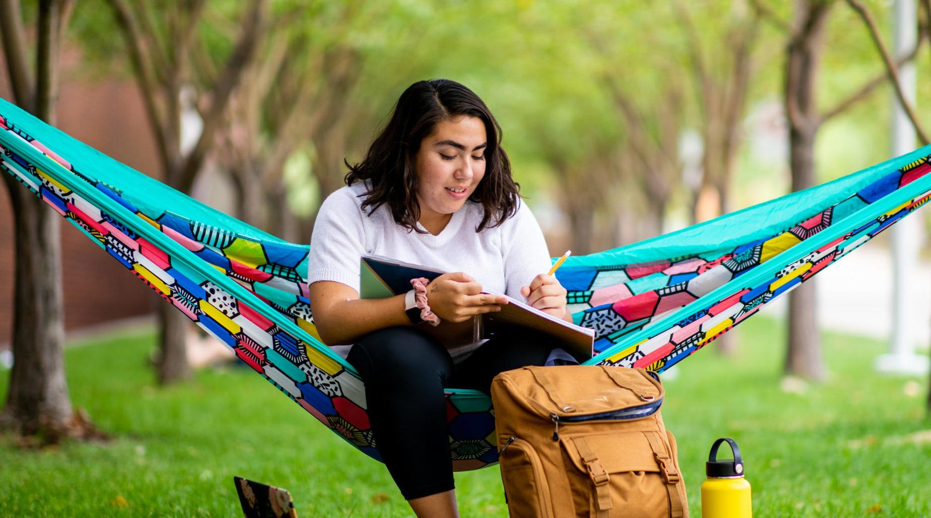 Student sitting in hamock outside on campus studying