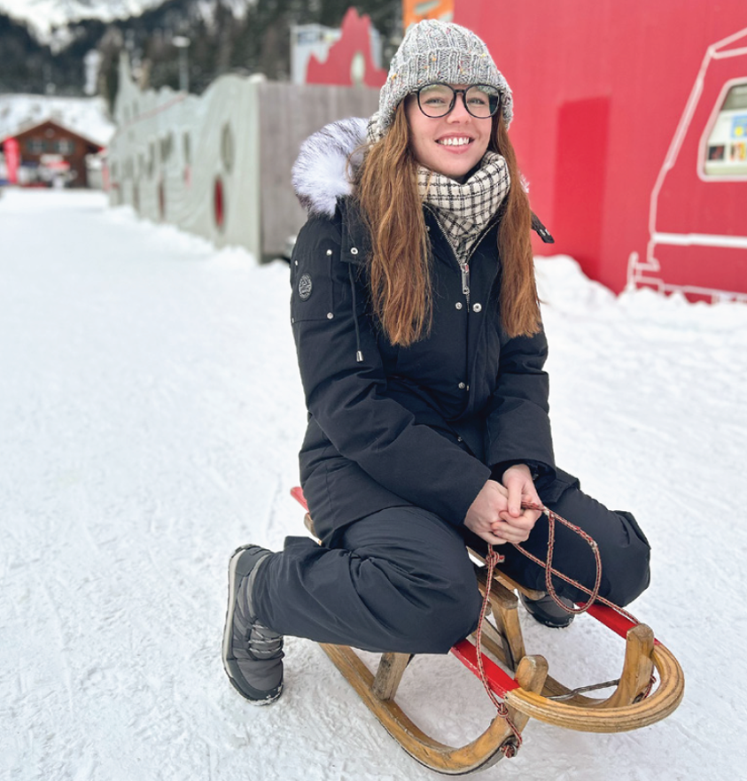 A student sitting on an old wooden sled in the snow.