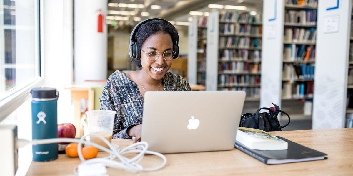 微笑的女学生在图书馆的MacBook上